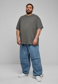 Graues, übergroßes T-Shirt mit Rundhalsausschnitt und kurzen Ärmeln, kombiniert mit hellblauen, lässigen Jeans; weiße Sneaker runden den Look ab.