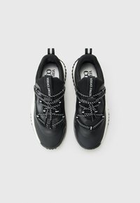 Črno-bele Versace Jeans težke tenisice z vzorčastimi vezalkami in blagovno znamko oznakami, prikazane na enostavni beli podlagi.