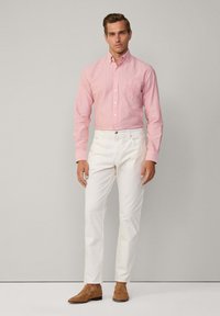 Camicia a righe rosse e bianche con bottoni, pantaloni bianchi e mocassini beige. La camicia presenta un colletto e maniche lunghe con polsini a bottoni.
