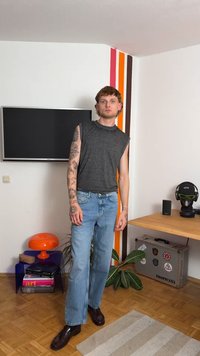 Gray sleeveless top, light blue wide-leg jeans, and dark shoes. Room with a TV, orange lamp, and plant. Colorful wall stripes in background.