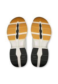 Les semelles de chaussures présentent une combinaison de caoutchouc orange et noir avec des motifs texturés. Une semelle intermédiaire blanche sépare les sections colorées pour un soutien et une adhérence.