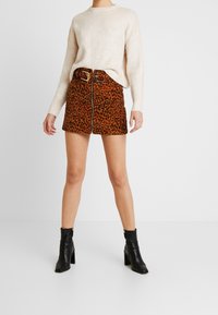 Brąskowa spódnica w panterkę z przednim zamkiem błyskawicznym i szlufkami na pasek, zestawiona z kremowym swetrem prążkowanym i czarnymi botkami za kostkę.