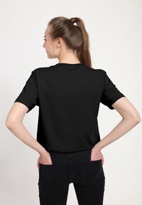 Černé tričko s krátkým rukávem v klasickém střihu, s kulatým výstřihem a hladkým bavlněným materiálem, stylizované s tmavými džíny.