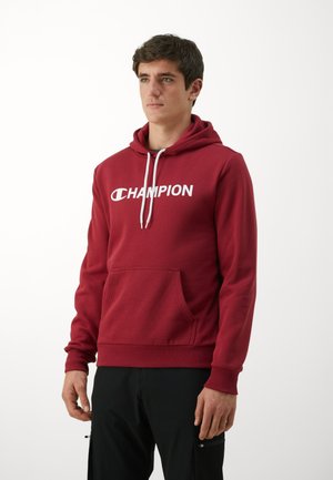 Roter Hoodie aus weichem Material mit einer Fronttasche, weißen Kordeln und einem großen weißen "CHAMPION"-Logo auf der Brust.