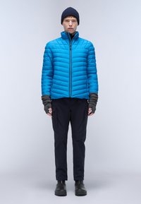 Giacca a vento blu brillante con design a righe orizzontali, colletto rialzato e zip frontale. Abbinata a pantaloni scuri e guanti senza dita.