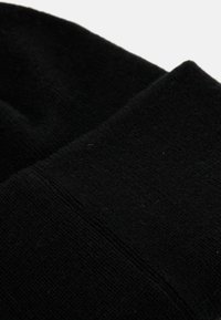 Berretto lavorato a maglia nero, con una texture morbida e un polsino a coste. Il materiale sembra leggero e presenta un colore uniforme in tutto il berretto.
