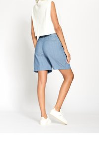 Světle modré denimové šortky s uvolněným střihem, vybavené bočními kapsami a hladkou strukturou. Nosené s krátkým bílým topem a teniskami.