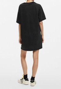 Czarna, oversize sukienka w t-shircie z krótkimi rękawami, okrągłym dekoltem i gładkiego bawełnianego materiału, w zestawie z białymi sneakersami z czarnymi akcentami.