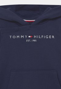 Námornícky modrá mikina s kapucňou vyrobená z bavlny s predným vreckom. Obsahuje vyšívané logo "TOMMY HILFIGER" a dátum "EST. 1985" v bielej farbe.