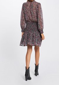 Blomstret kjole i transparent stof, med smocket talje, lange pufærmer og en flagrende nederdel. Bæret med sorte hælede ankelstøvler.