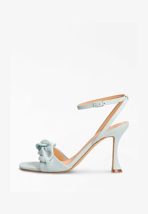 Jasnoniebieski sandał na wysokim obcasie z gładkiej skóry, ozdobiony kokardą na palcach i cienkim paskiem wokół kostki z klamrą.