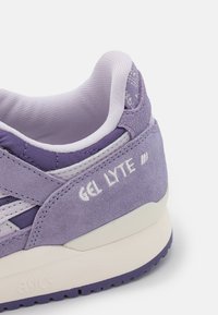 Fialová sportovní bota z semiše a síťoviny s krémovou podrážkou, na které je bílé nápis „GEL LYTE“ a výrazné švy na patě.