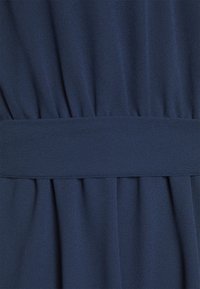 Navy blue kangas leno zilishe, iliyo na sura ya kipekee, ikiwa na mikunjo na ukanda mpana. Nyenzo hiyo ni laini yenye mwangaza kidogo.