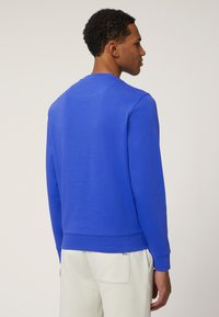 Royalblauwe sweatshirt met een ronde hals, gladde textuur, lange mouwen en geribbelde manchetten. Heeft een iets gebogen achterkant.