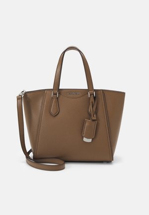 Sac fourre-tout en cuir marron avec poignées doubles, bandoulière détachable et étiquette à bagages rectangulaire sur fond blanc.