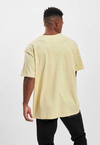 Gul overdimensioneret bomulds T-shirt med korte ærmer, glat tekstur og en afslappet pasform, parret med sorte bukser. Minimalistisk design.