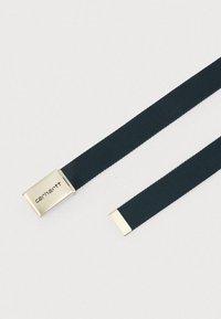 Cinturón de tela negra tejido con hebilla rectangular plateada grabada con el nombre de la marca Carhartt y punta del cinturón plateada sobre un fondo blanco.