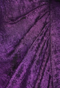 Blødt, tekstureret lilla stof med en glansfuld finish, der viser diagonale folder og subtile variationer i skygge og glans.