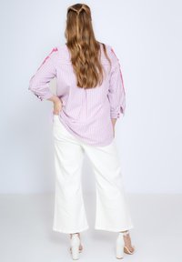 Gestreept shirt in roze en wit, met knoopdetails en driekwart mouwen. Gepaard met witte broek met wijdbeen en blokhak schoenen.