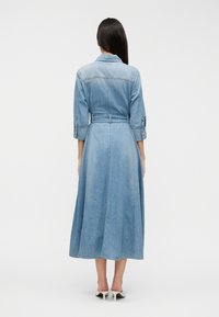 Φόρεμα από ανοιχτό μπλε τζιν με μήκος μέχρι τη μέση της γάμπας, κουμπιά μπροστά, ρυθμιζόμενη ζώνη στη μέση και γυρισμένα μανίκια. Λείος υφής.
