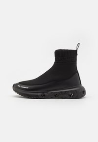 Bottine noire avec un dessus en tricot texturé, dotée d'un poignet à côtes et d'une semelle en caoutchouc épaisse avec des motifs géométriques et un détail de logo.