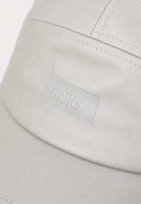 Lichtgrijze honkbalpet gemaakt van een glad, waterdicht materiaal, met een voorlabel waarop de blindgeperste tekst "RAINS" staat.