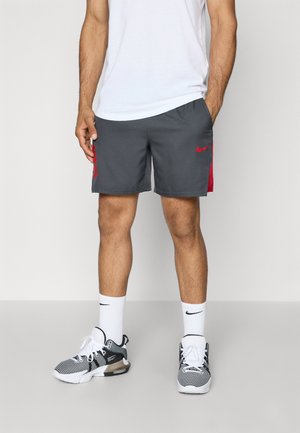Grey sports shorts with red accents and a side logo, crafted from breathable material. Paired with black and white athletic shoes and white socks.