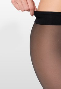 Czarne, przejrzyste rajstopy z szerokim, gładkim czarnym pasem w talii, prezentujące gładką, przezroczystą fakturę i naturalny odcień skóry pod spodem.