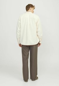 Camicia in corda chiara a maniche lunghe con vestibilità comoda, polsini a bottone e orlo dritto sul retro, abbinata a pantaloni larghi marroni.