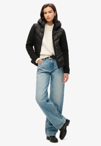 Chaqueta de abrigo negra con capucha, suéter crema debajo, jeans claros de corte suelto, cinturón negro y botas negras. Diseño sencillo y ajuste relajado.