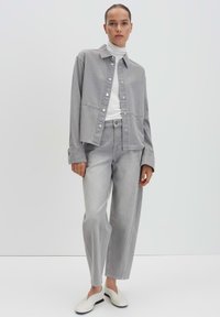 Gray denim jacket with matching gray pants, featuring a button-up front, wide legs, and a relaxed fit. Worn with white slip-on shoes.