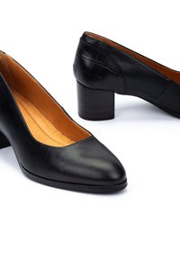 Pompes noires en cuir avec un bout pointu et un petit talon en bloc texturé. L'intérieur présente une doublure en cuir beige. Détail en relief crocodile à l'arrière.