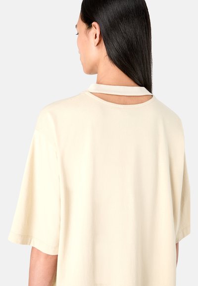 Beige, short-sleeve T-shirt with a round neckline and an open back detail. Made of soft fabric with a smooth texture.