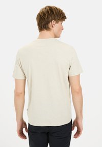 Beiges T-Shirt mit kurzem Arm und Rundhalsausschnitt, aus weichem Stoff gefertigt. Hat einen geraden Schnitt und ein dezentes Logodetail an der Seite.