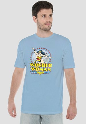 Man wearing light blue T-shirt with vintage Wonder Woman graphic in red, yellow, and blue colors on front, looking to his right.