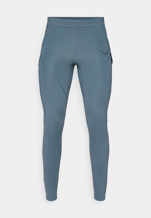 Leggings deportivos azules con una textura suave, cuentan con bolsillos laterales y un logo negro en contraste en la cadera. Diseño ajustado.