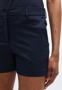 Σορτς ναυτικού μπλε κατασκευασμένα από ελαφρύ ύφασμα, με επίπεδη μπροστινή όψη, πλαϊνή τσέπη με φερμουάρ και διακριτική λεπτομέρεια λογότυπου στο τελείωμα.