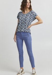 Volné tričko s květinovým vzorem v modré barvě, s krátkými rukávy. Úzké modré kalhoty s knoflíkovými detaily na bocích, doplněné lehkými polovysokými teniskami.