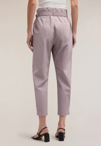 Lichtpaarse broek met hoge taille en riem, voorzien van een taps toelopende pijp en een cropped lengte. Glad materiaal en minimale stikseldetails.
