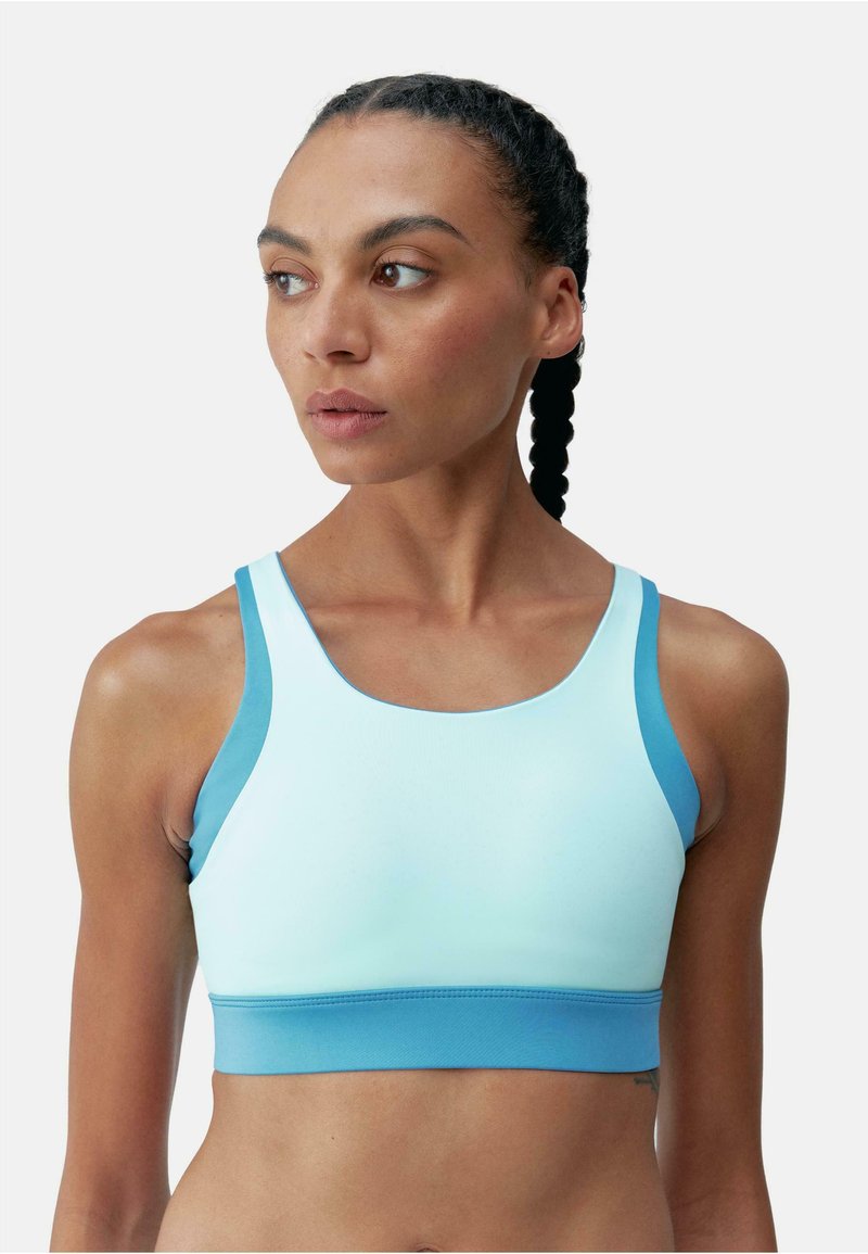 Sutien sport de culoare albastru deschis, cu bretele ajustabile, realizat dintr-un material elastic. Prezintă o bandă solidă de culoare turcoaz și o textură netedă.