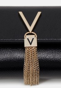 Mustan nahkainen clutch, jossa on kultainen "V"-logo ja kultaketjuinen tupsu. Raitapintainen pinta lisää visuaalista mielenkiintoa.