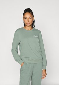 Lysegrønn genser med rund hals og ribbestrikkede mansjetter, med en hvit "LIMITLESS"-logo på brystet og mykt bomullsstoff.