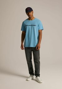 Jasnoniebieska bawełniana koszulka z czarnym napisem "diverse", w połączeniu z ciemnoszarymi dżinsami i białymi sneakersami. Czapka w kolorze granatowym z czerwonym napisem.