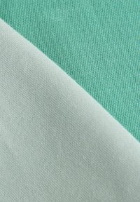 Close-up of folded fabric showing a light green knit side and a white smooth side with visible textile textures.