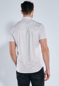 Hemd mit kurzen Ärmeln in Hellgrau mit einem subtilen strukturierten Muster, mit Button-Down-Kragen und einer lockeren Passform, kombiniert mit dunklen Jeans.