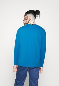 Blaues Baumwollhemd mit langen Ärmeln, Rundhalsausschnitt und geradem Saum, kombiniert mit dunkelblauen Hosen. Keine sichtbaren Muster oder Akzente.