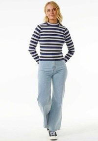 Gestreiftes Langarmshirt in Marineblau, Schwarz und Hellblau, kombiniert mit hellblauen weit geschnittenen Jeans und schwarzen Turnschuhen.