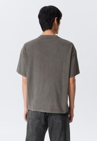 Ruskea, lyhythihainen T-paita rentoutuneella istuvuudella ja pyöreällä pääntiellä; siinä on pehmeä pinta ja hieman haalistunut viimeistely.