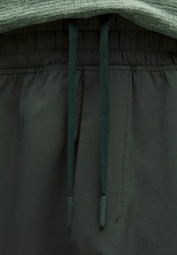 Mörkgrå sportshorts med en samlad elastisk midja, som har gröna dragsko med plasttoppar och ett slätt, lättviktigt tyg.