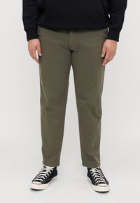 Khaki chinos sirge lõikega, koos mustade kõrge säärega tossudega. Materjal on sile ja klassikalise nelja taskuga disainiga.